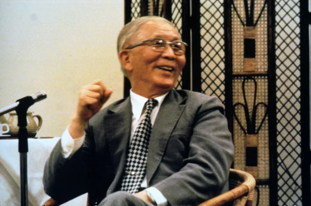 Witness Lee seated beside a microphone while speaking